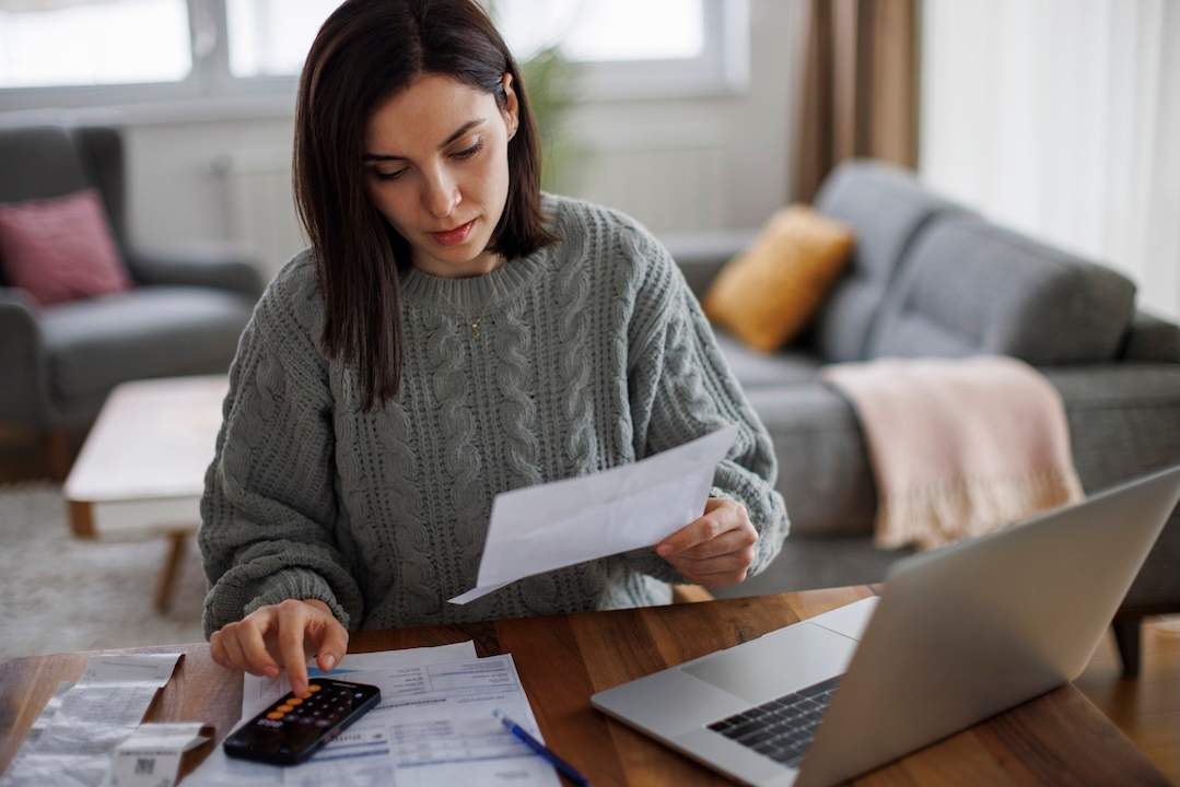 Person paying bills using calculator and laptop